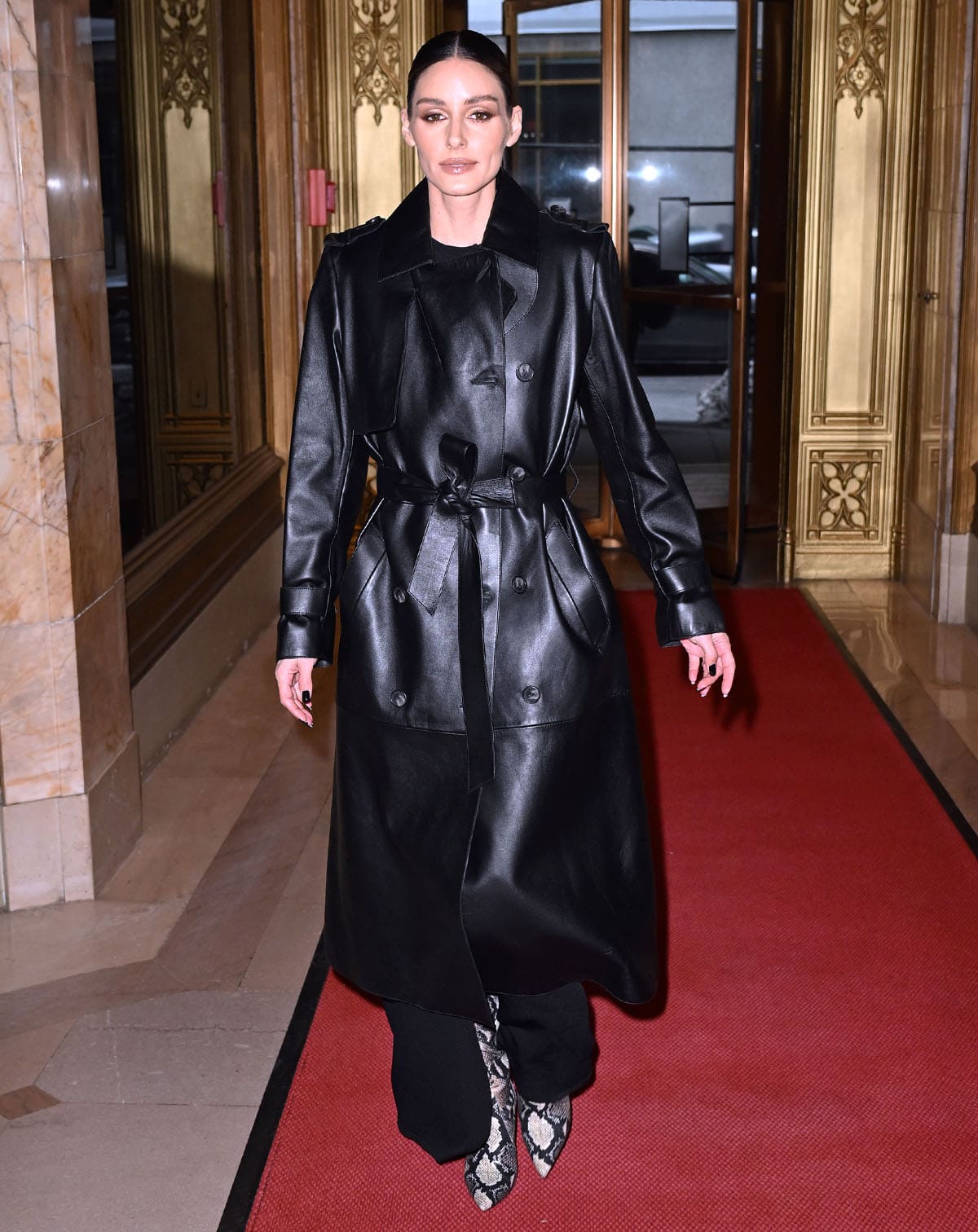 Olivia Palermo sharpens her all-black look with pointed snakeskin boots, adding texture and contrast to a sleek black leather coat layered over an ankle-length LBD