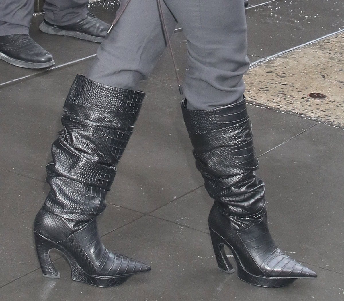 Priyanka Chopra wears the striking Thom Solo Patchwork Curved boots in black croc-embossed leather featuring curved heels, wedged-cut platforms, and pointed toes