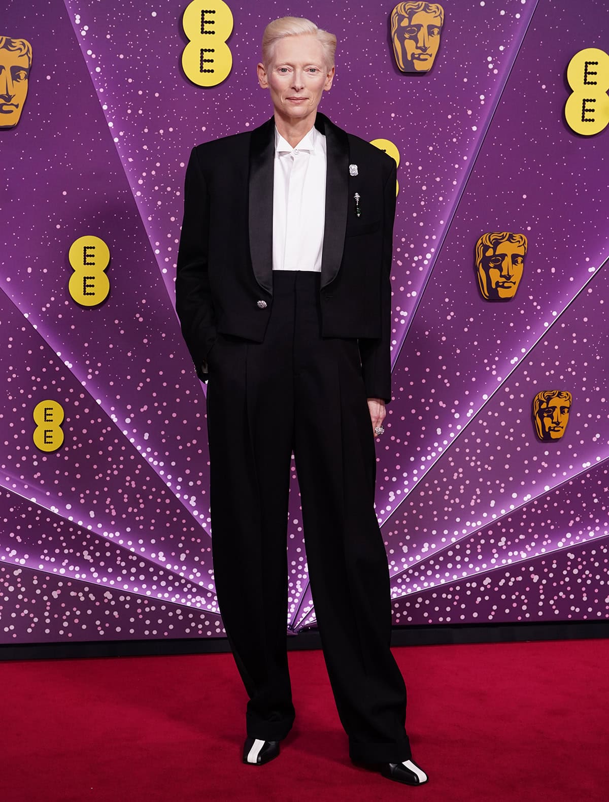 Tilda Swinton embraces androgynous tailoring, wearing a Chanel cropped tuxedo jacket, a white shirt, and high-waisted black trousers