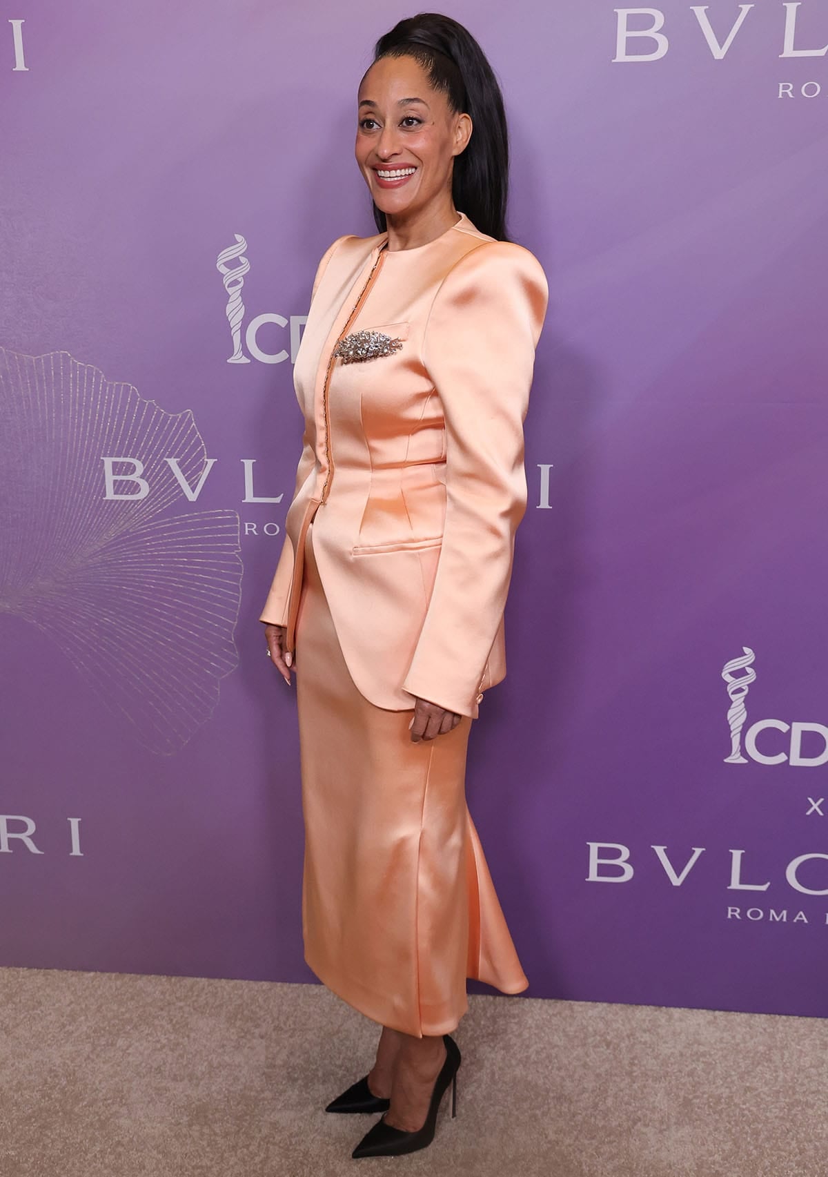 Tracee Ellis Ross puts a fresh spin on red-carpet tailoring with a peach Mugler skirt suit featuring a jacket with structured shoulders and a brooch on the chest pocket, and a midi skirt