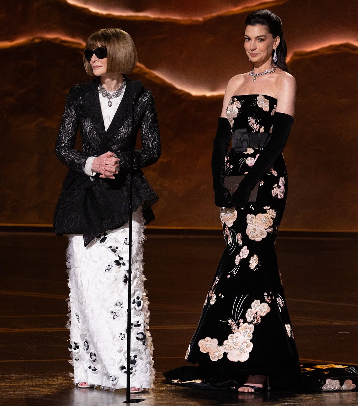 Anne Hathaway, on stage with Anna Wintour, stuns in her Old Hollywood look, featuring a black floral Valentino gown and Roger Vivier heels