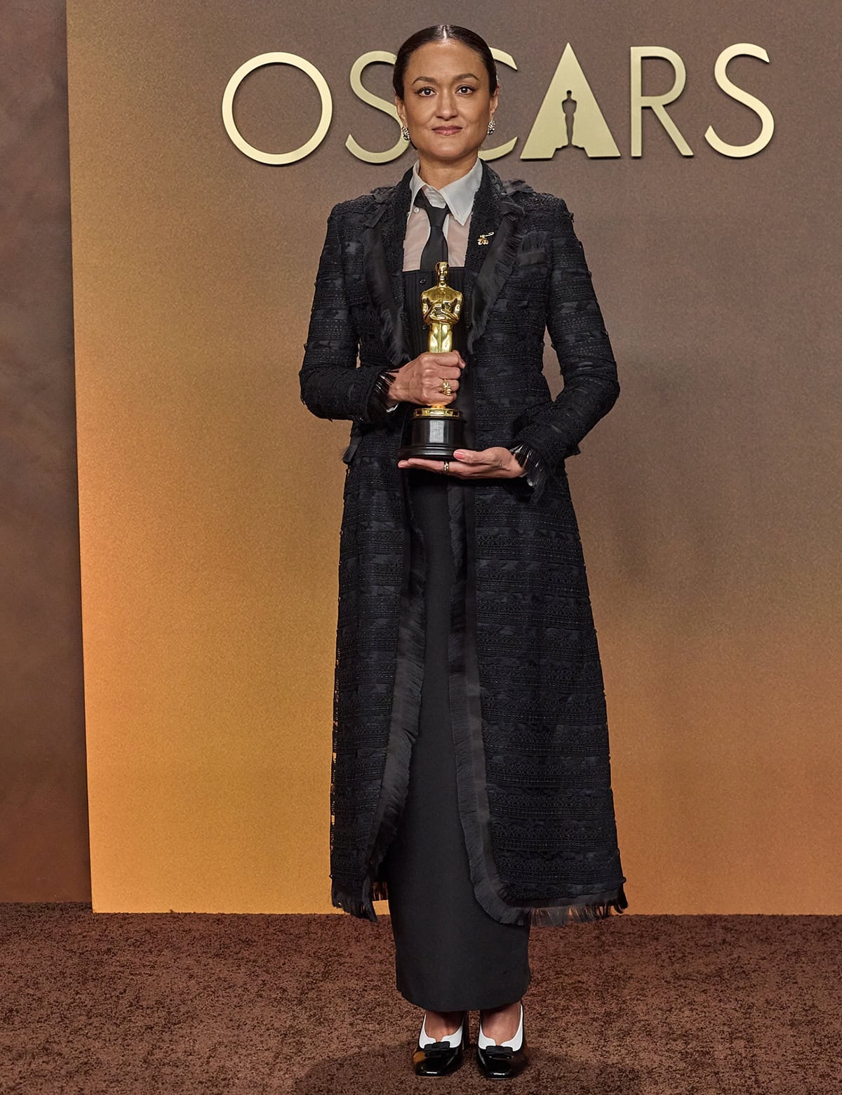 Autumn Durald Arkapaw pairs her oxford-inspired pumps with a full Thom Browne look featuring an intricately embroidered black coat, a white shirt underneath, a black tie, and a column skirt