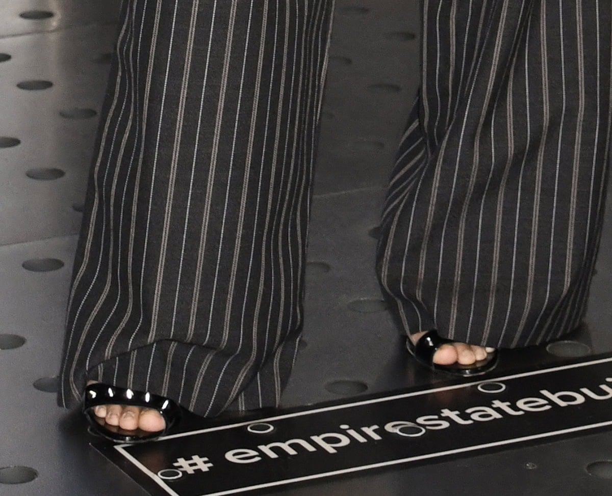 Avantika Vandanapu adds tough-chic edge to business dressing with the DSquared2 “Gothic” sandals in shiny black patent leather with silver-tone spike studs