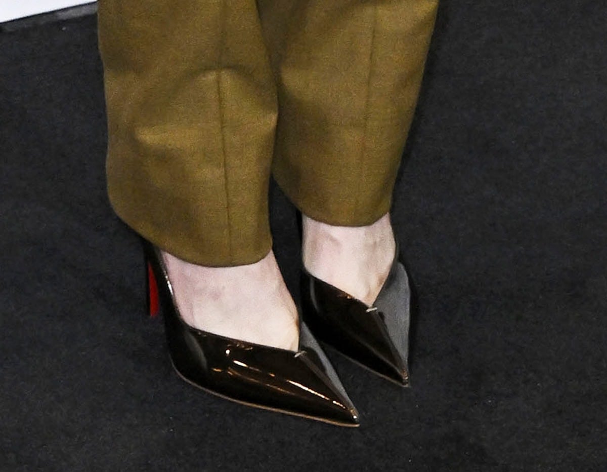 Greta Gerwig opts for sharp tailoring with the Christian Louboutin ”Erozee” pumps in glossy black patent leather with V-shaped vamps, pointed toes, and stiletto heels