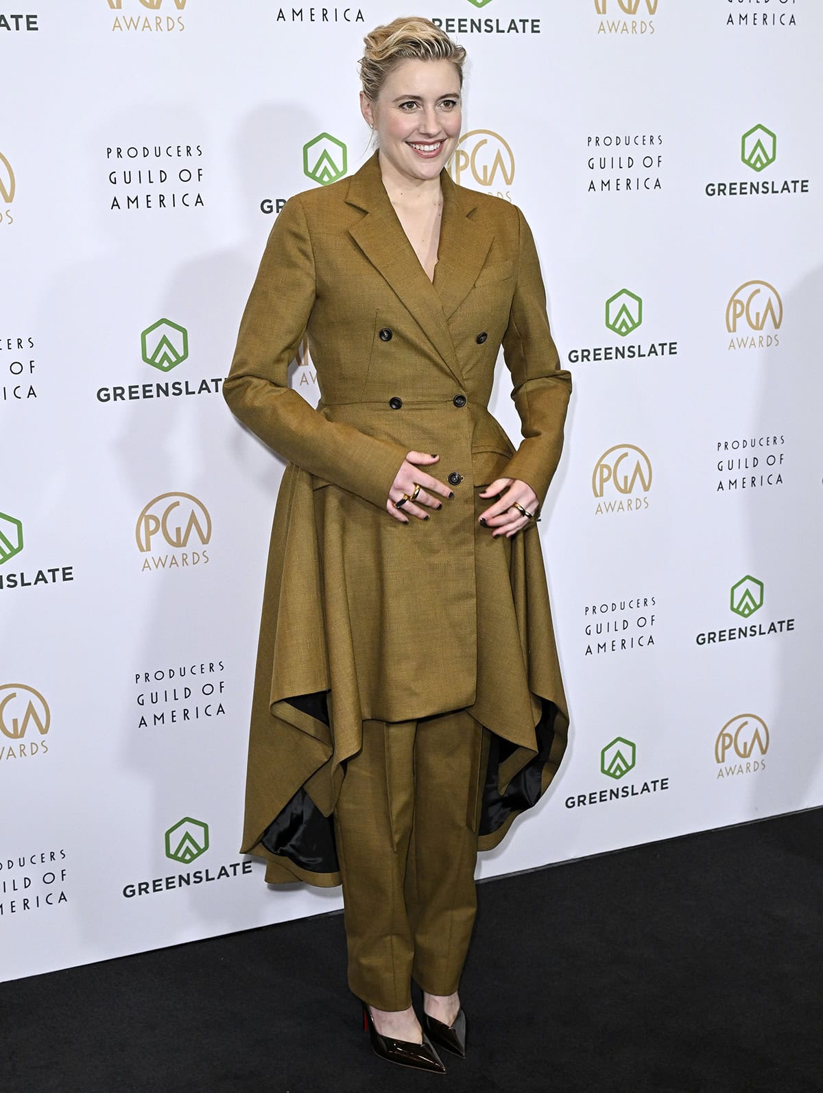 Greta Gerwig pairs her Louboutins with an olive-green set from Diotima, featuring a double-breasted wool-blend riding coat and matching straight-leg trousers with a skirt overlay