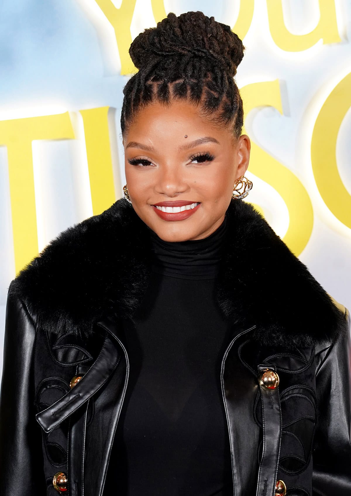 Halle Bailey completes her look with Alexis Bittar earrings, a sculpted high bun, and soft glam defined by fluttery lashes and a bold red lip