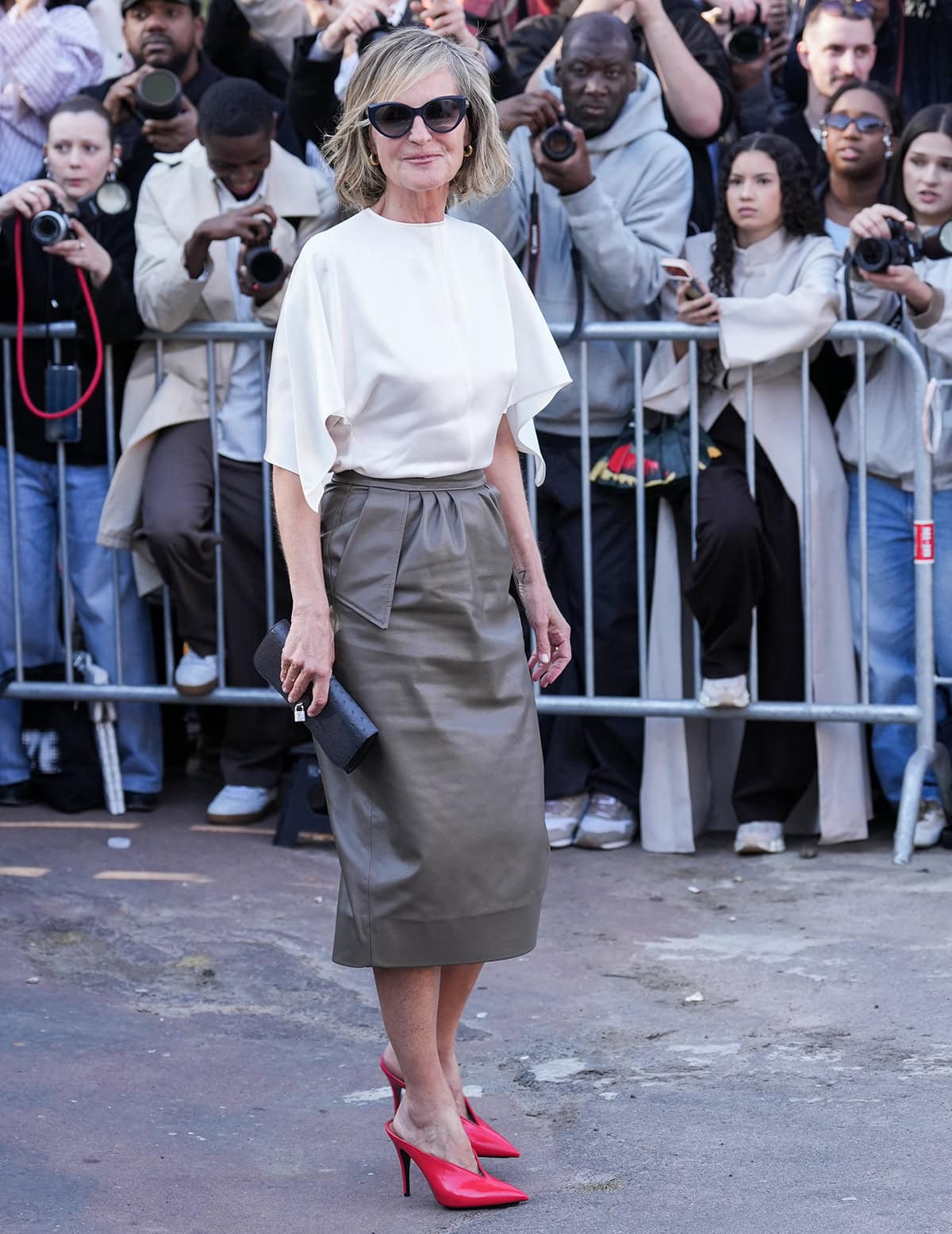 Helen Hunt lets her glossy red pointed-toe mules steal the spotlight, pairing the bold heels with a flowing white blouse and a sleek gray pencil midi skirt