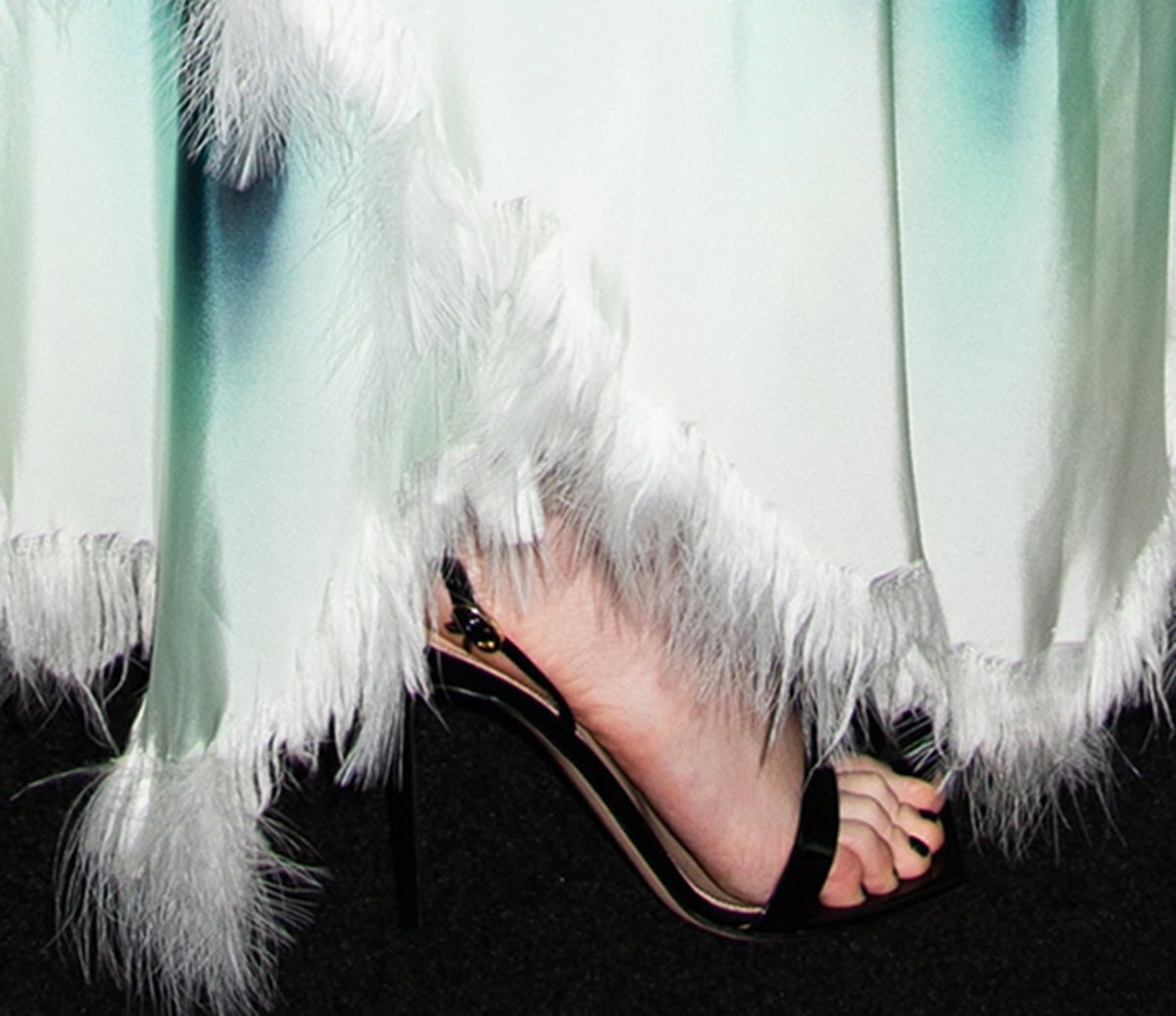 Jessie Buckley slips her black-pedicured feet into Gianvito Rossi's Ribbon sandals featuring a strap across the toe, an ankle strap with a gold-tone ribbon buckle, and stiletto heels