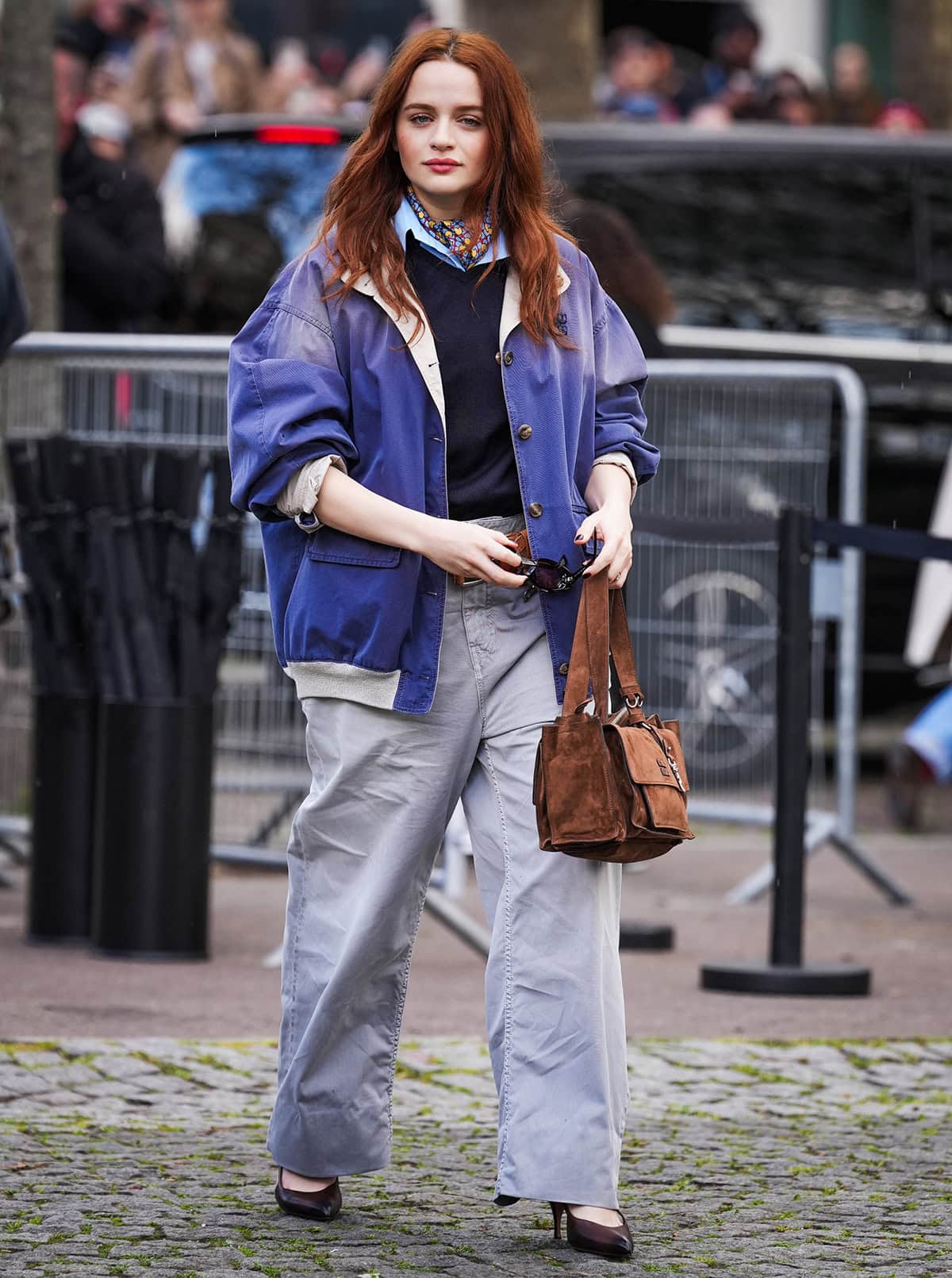 Joey King pairs her dark brown hand-waxed pumps with pants, a navy vest, a light blue collared shirt, and a blue jacket