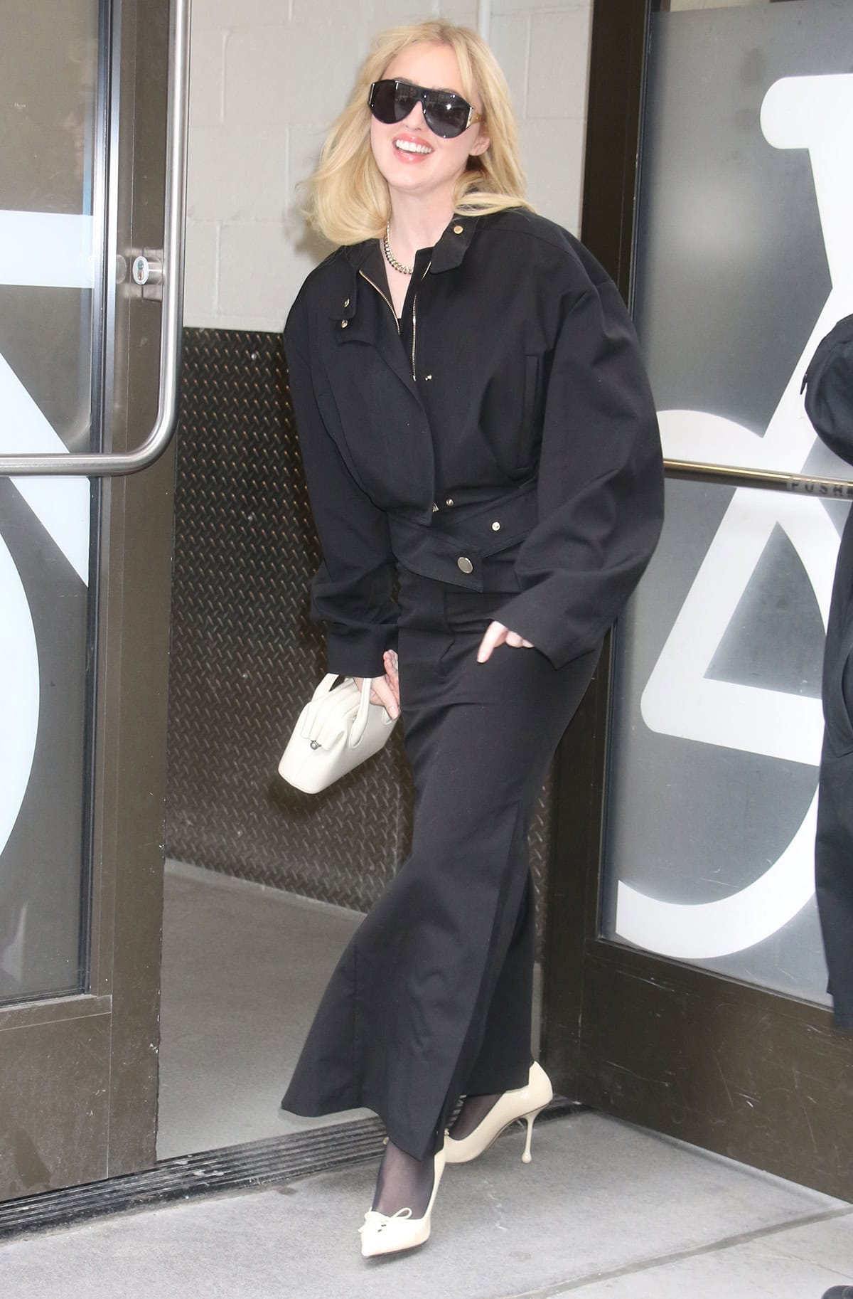 Kathryn Newton pairs white Jimmy Choo “Scarlett” pumps with a structured Sportmax jacket and long skirt set, styled with sheer tights and a mini top-handle bag