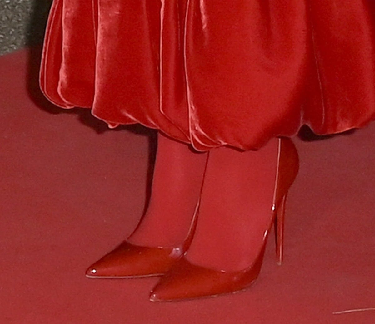 Kathryn Newton slips into a pair of shiny red Christian Louboutin “So Kate” pumps and daring red tights