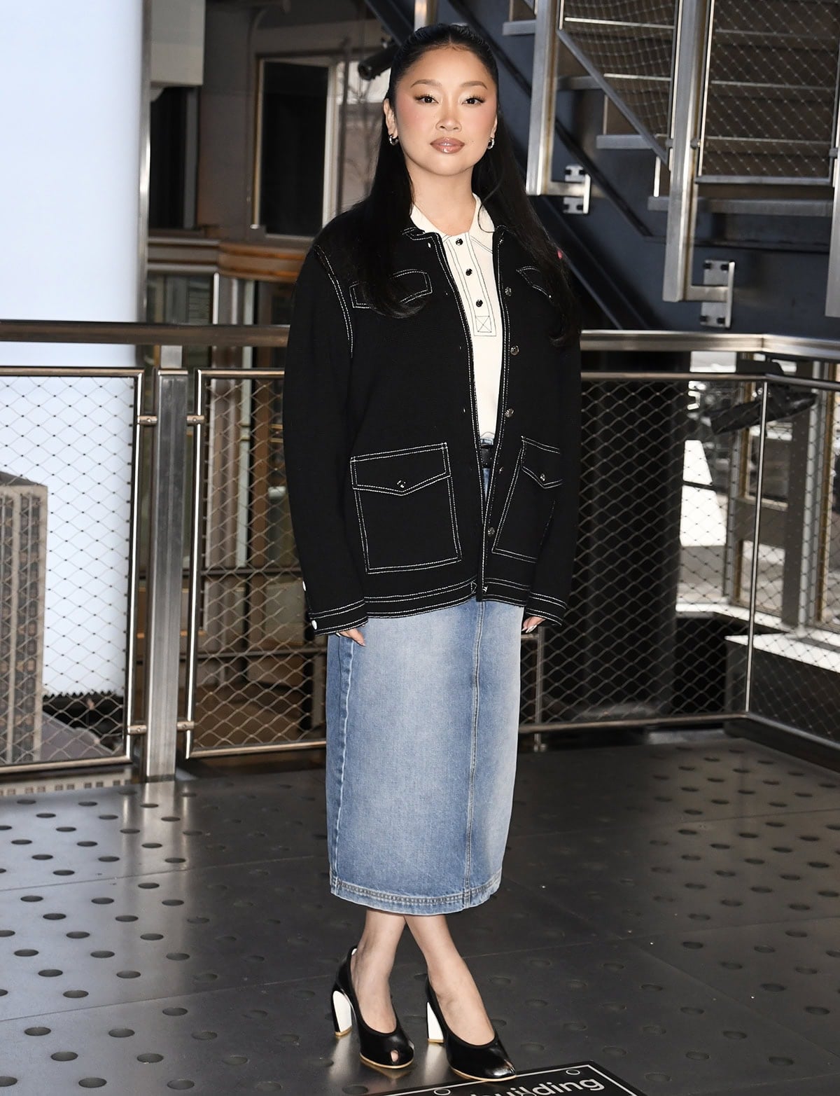 Lana Condor pairs her sculptural black pumps with a Tory Burch ensemble, featuring a light wash denim midi skirt, a white polo with contrast black topstitching, and an oversized black jacket with white topstitching