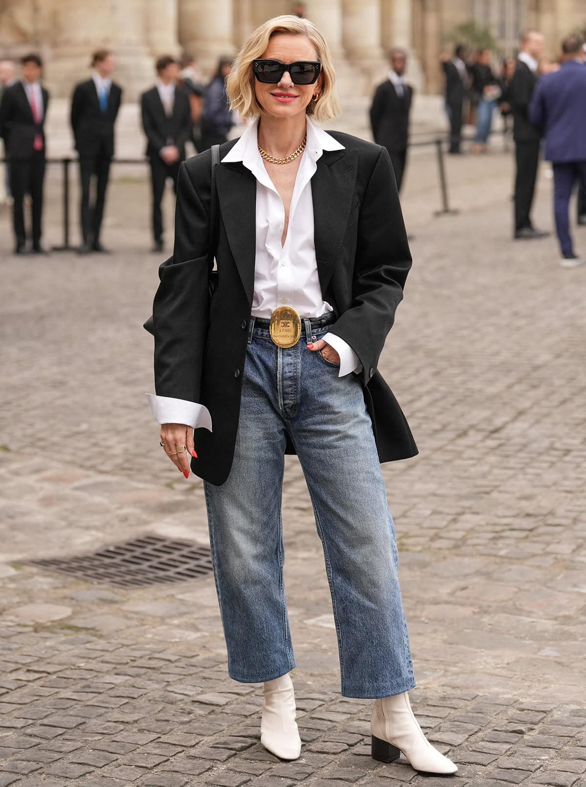 Naomi Watts pairs her white boots with a crisp white blouse, an oversized black blazer, and straight-leg crop jeans with Celine's black leather belt and oversized gold-tone collar stud