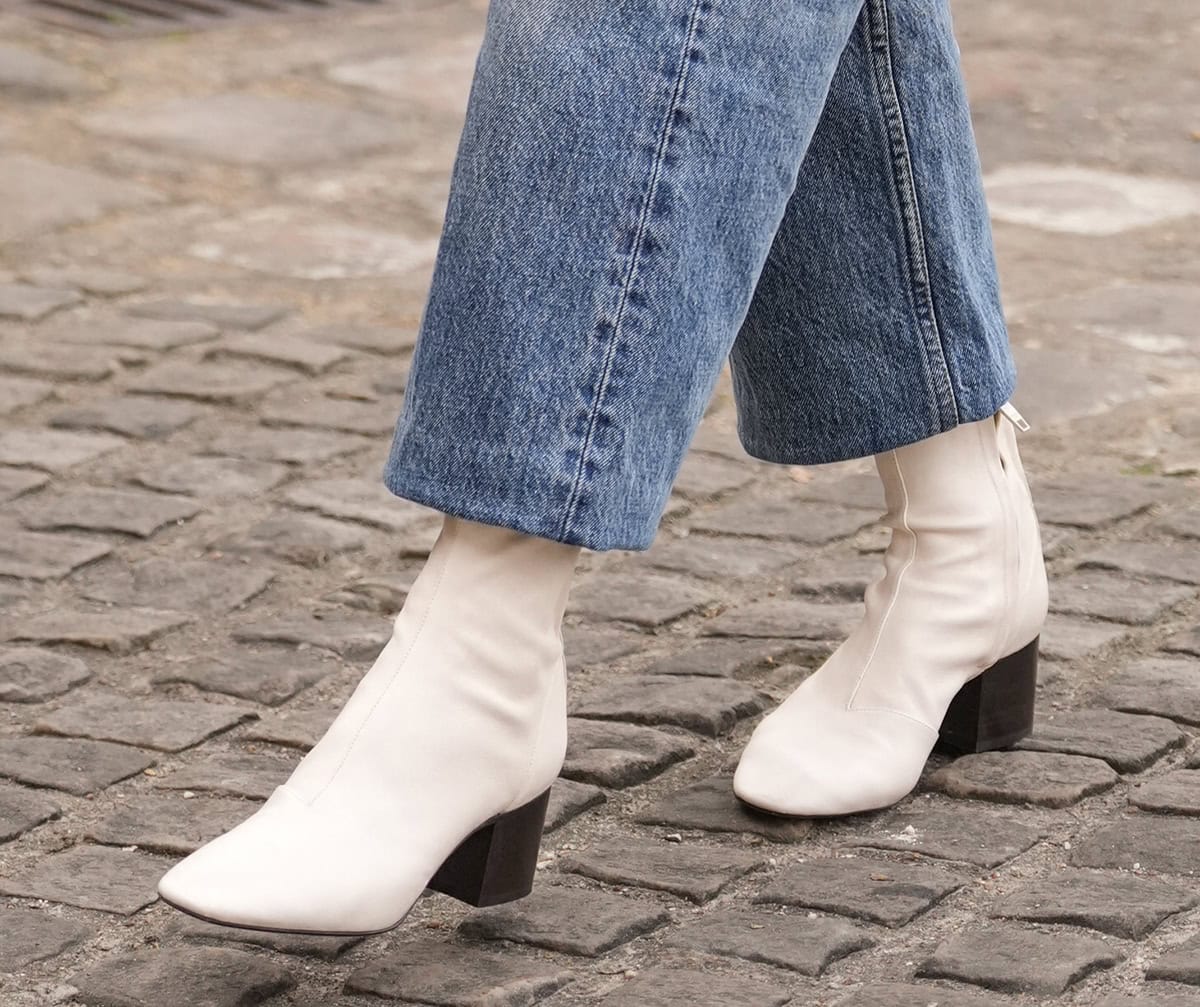 Naomi Watts wears the white Celine “Cheri” boots, made from lambskin leather with visible stitched panels, side zips, almond toes, and squared stacked leather heels