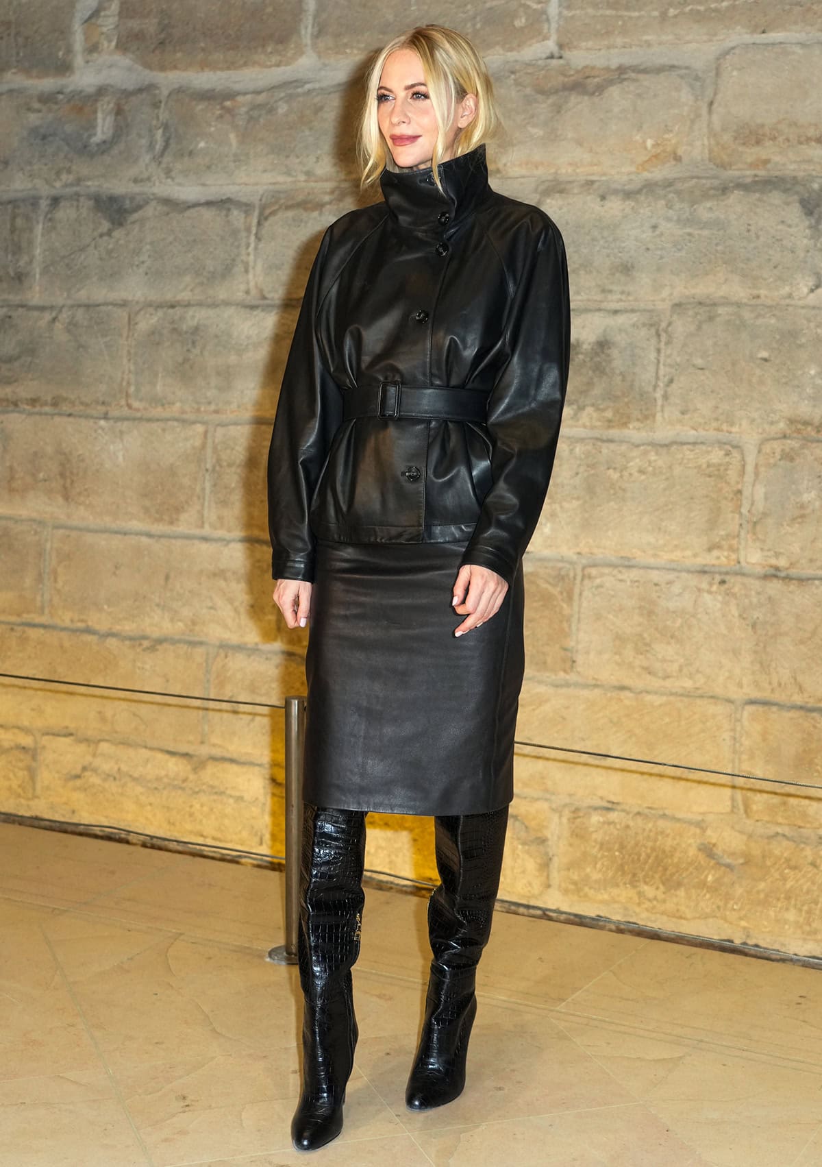 Poppy Delevingne keeps her look sleek, pairing her boots with a black pencil mini skirt and a black jacket with a turtleneck and tonal buckled belt