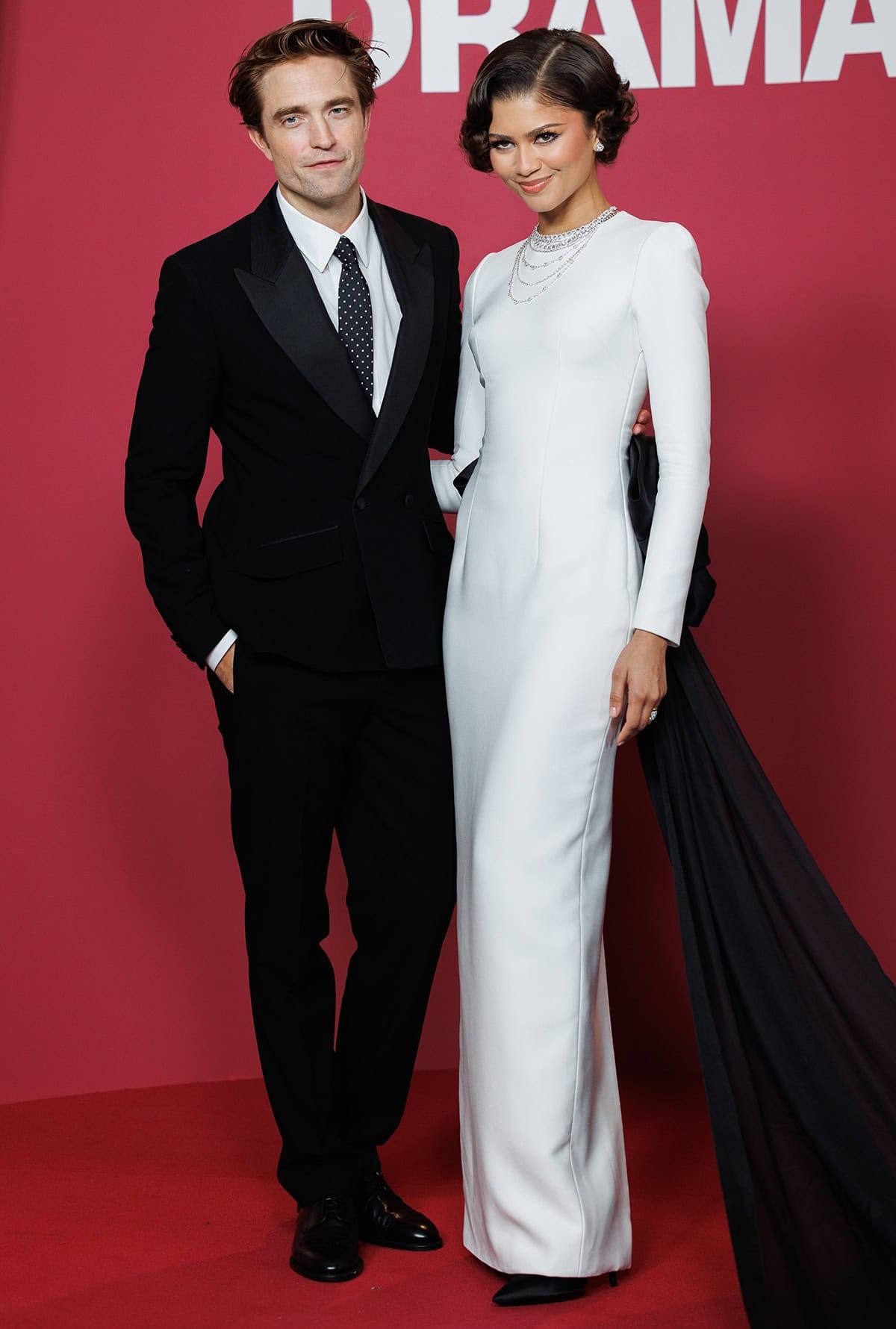Zendaya pairs a sculpted white gown with a dramatic black train and sharp black pointed-toe pumps while posing alongside Robert Pattinson at The Drama Paris premiere
