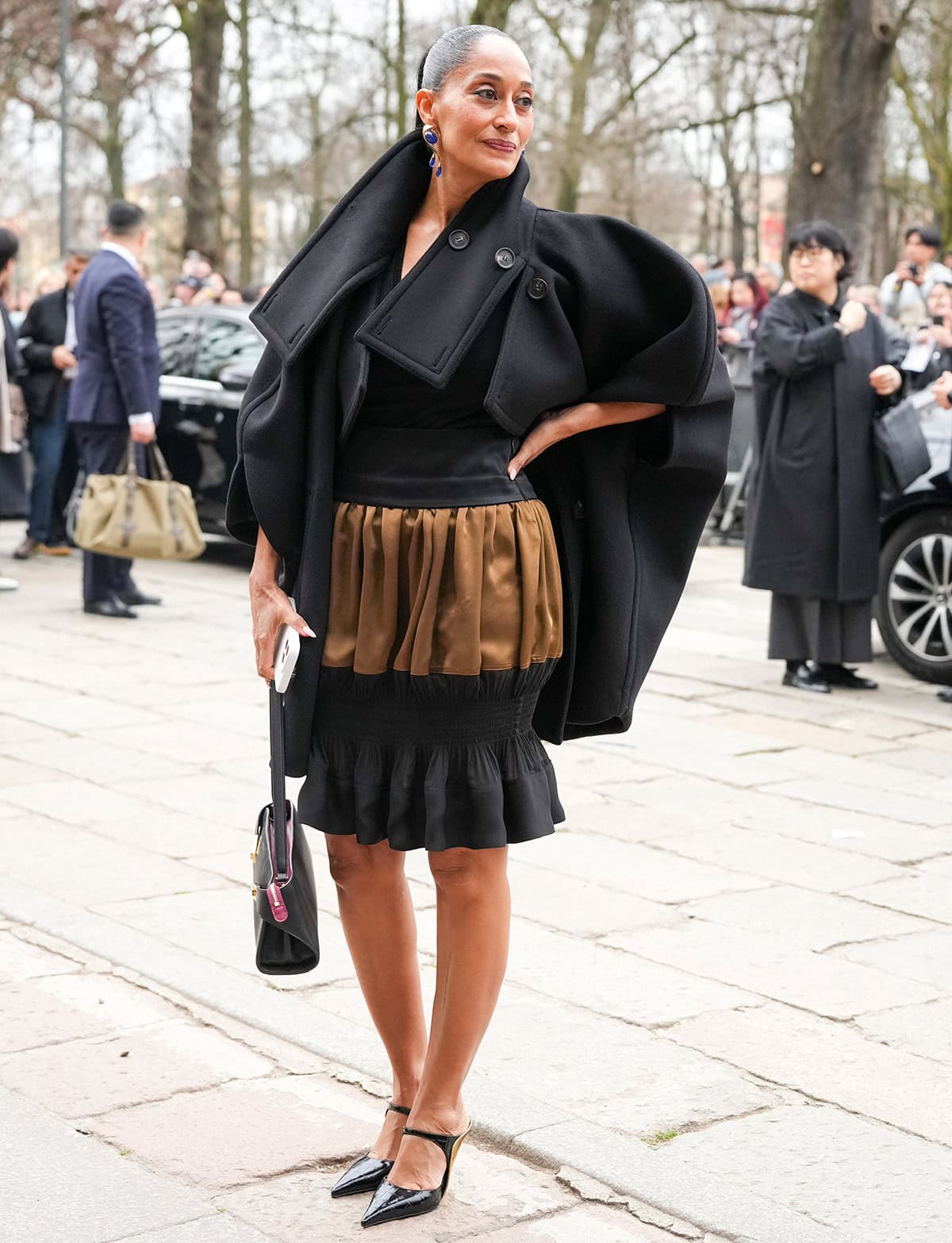 Tracee Ellis Ross pairs her two-tone croc leather mules with a black and brown bubble skirt, a black top, and a black coat
