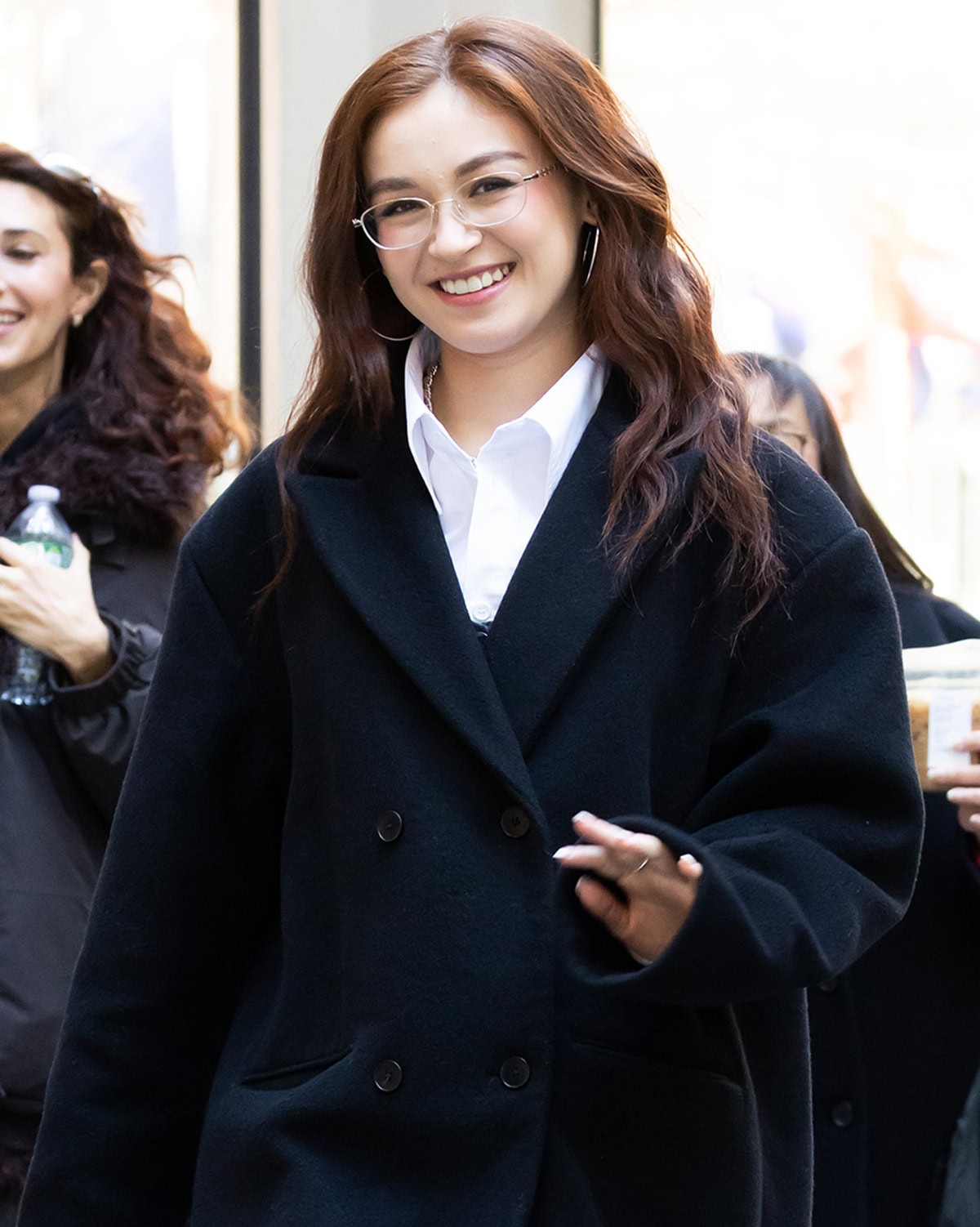 Anna Cathcart completes her polished, schoolgirl-inspired look with slim eyeglasses, oversized silver hoops, and softly tousled waves, striking a balance between studious charm and effortless off-duty glamour