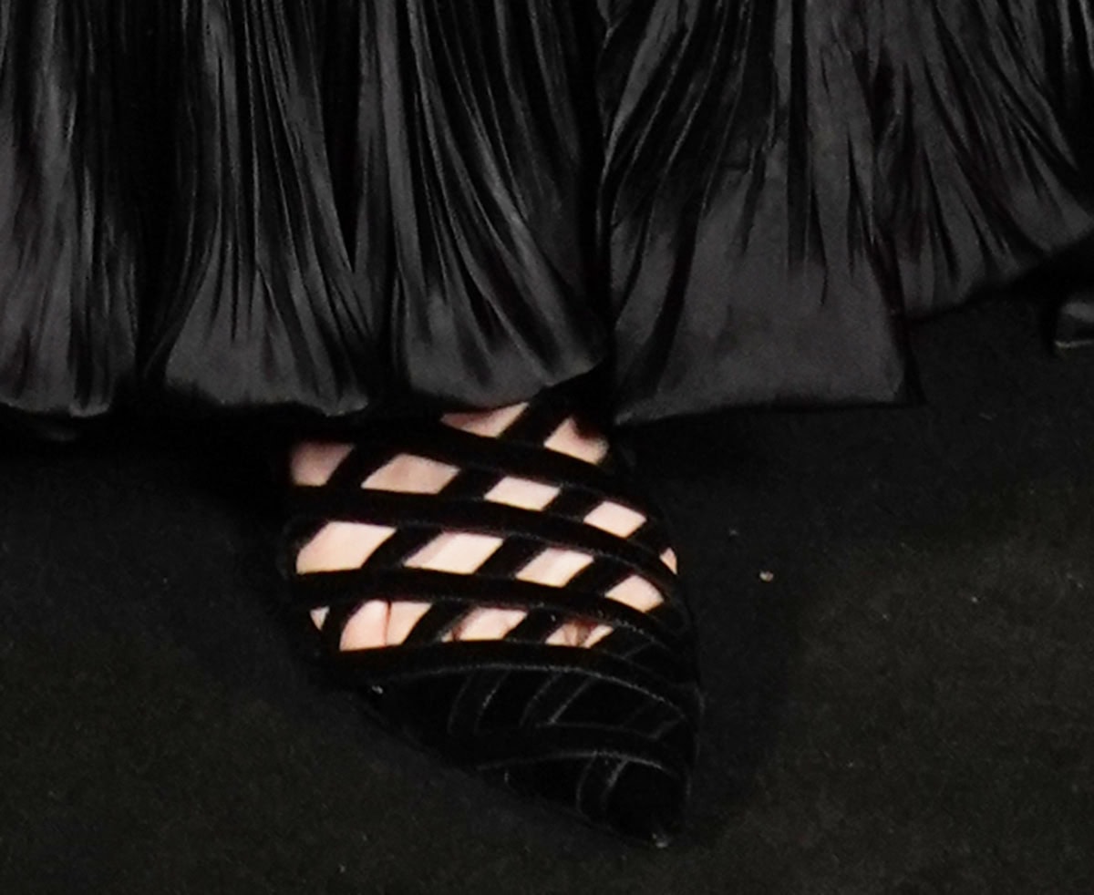 Anne Hathaway slips into a pair of black velvet Aquazzura “Romance” booties featuring a caged cutout design, pointed toes, and high heels