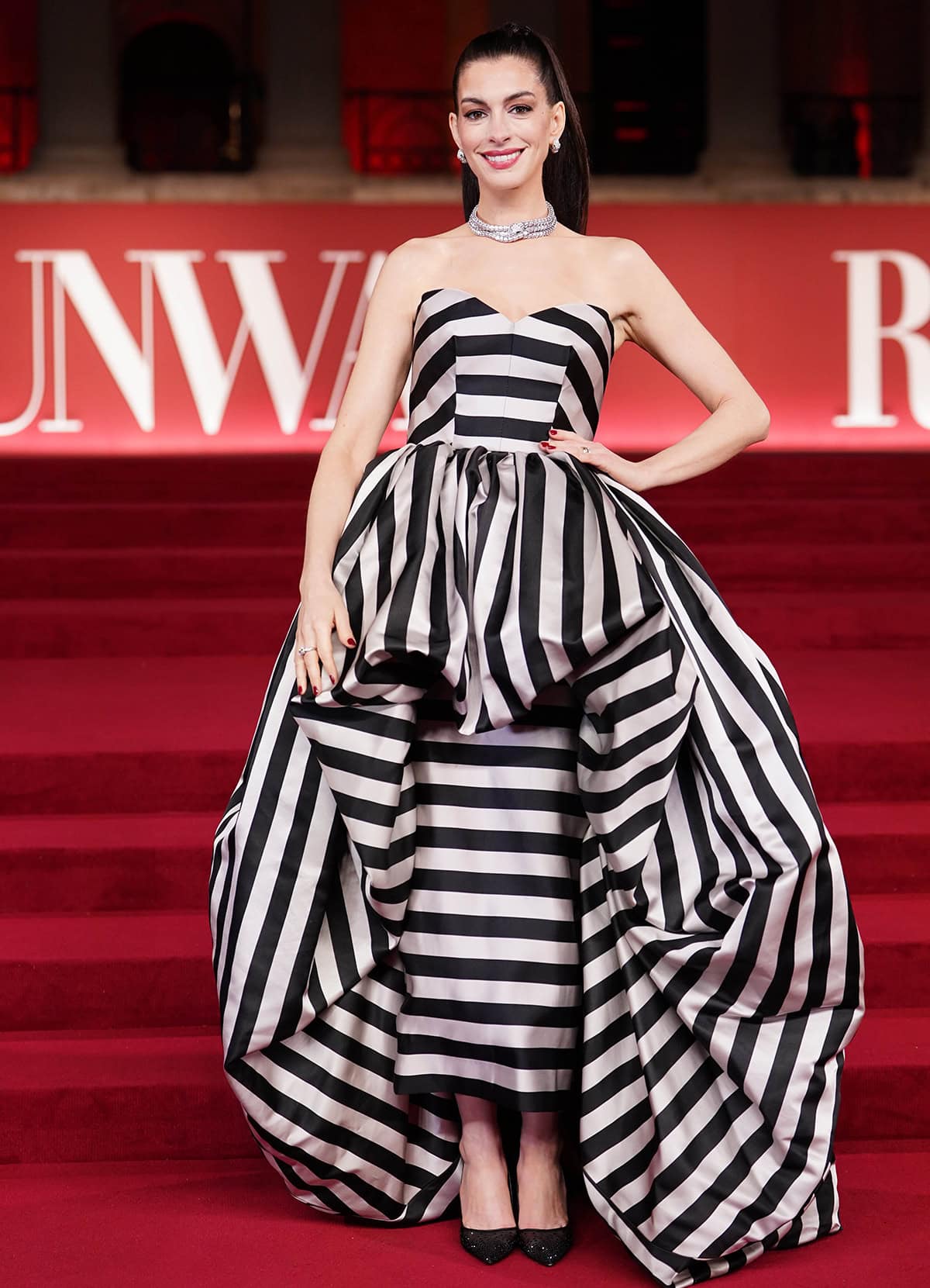 Anne Hathaway pairs her crystal mesh pumps with a bold, striped Louis Vuitton gown featuring a strapless sweetheart neckline, a column skirt underneath, and a voluminous bubble skirt overlay