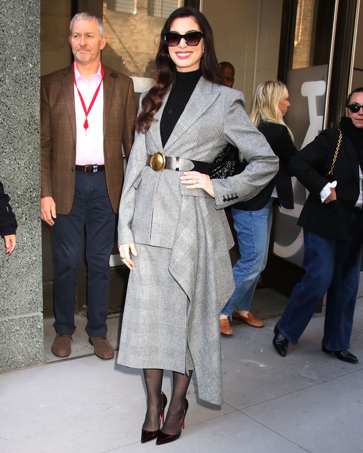 Anne Hathaway pairs her burgundy pumps with sheer black tights and a gray plaid Michael Kors skirt suit with a black bodysuit underneath
