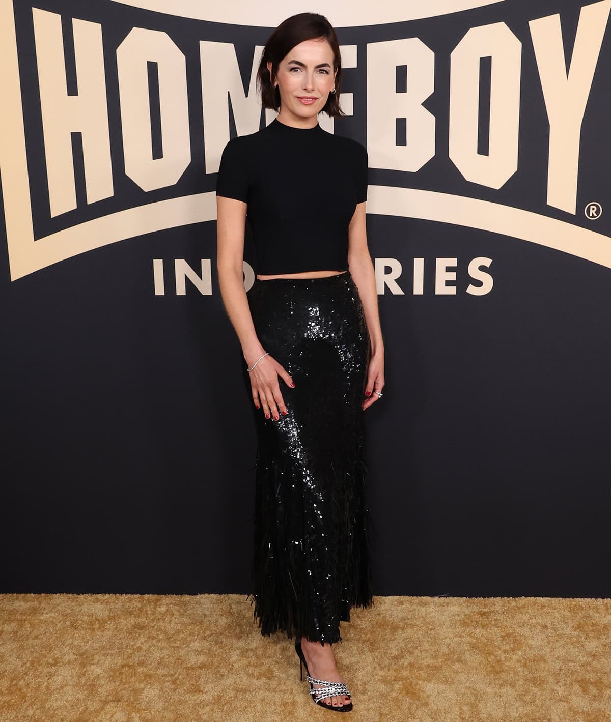 Camilla Belle pairs her crystal heels with a black Ralph Lauren crop tee and a black sequin-embellished skirt with a fringed hem