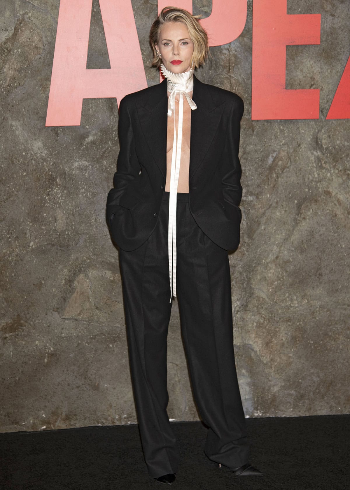 Charlize Theron pairs her satin pumps with black trousers and a single-breasted blazer, finished with a white Elizabethan-style collar tied with a long ribbon