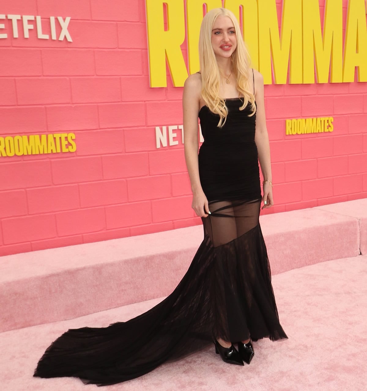 Chloe Cherry embraces sultry glamour, pairing sharp black pumps with a sheer black tulle Blumarine dress finished with a dramatic trailing hem