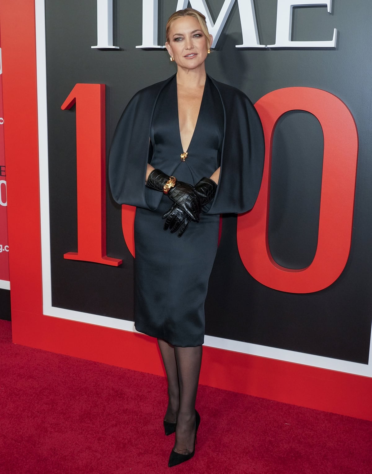 Kate Hudson teams her classic heels with a retro-style Khaite dress featuring voluminous, sculptural sleeves, a plunging neckline with a gold-tone brooch, and a pencil skirt