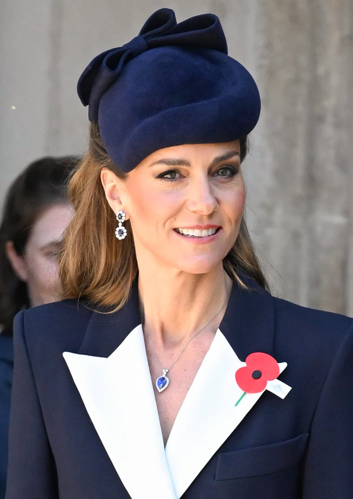 Catherine, Princess of Wales, finishes her look with a sculptural, navy Jane Taylor London fascinator, sapphire drop earrings, and a matching pendant necklace
