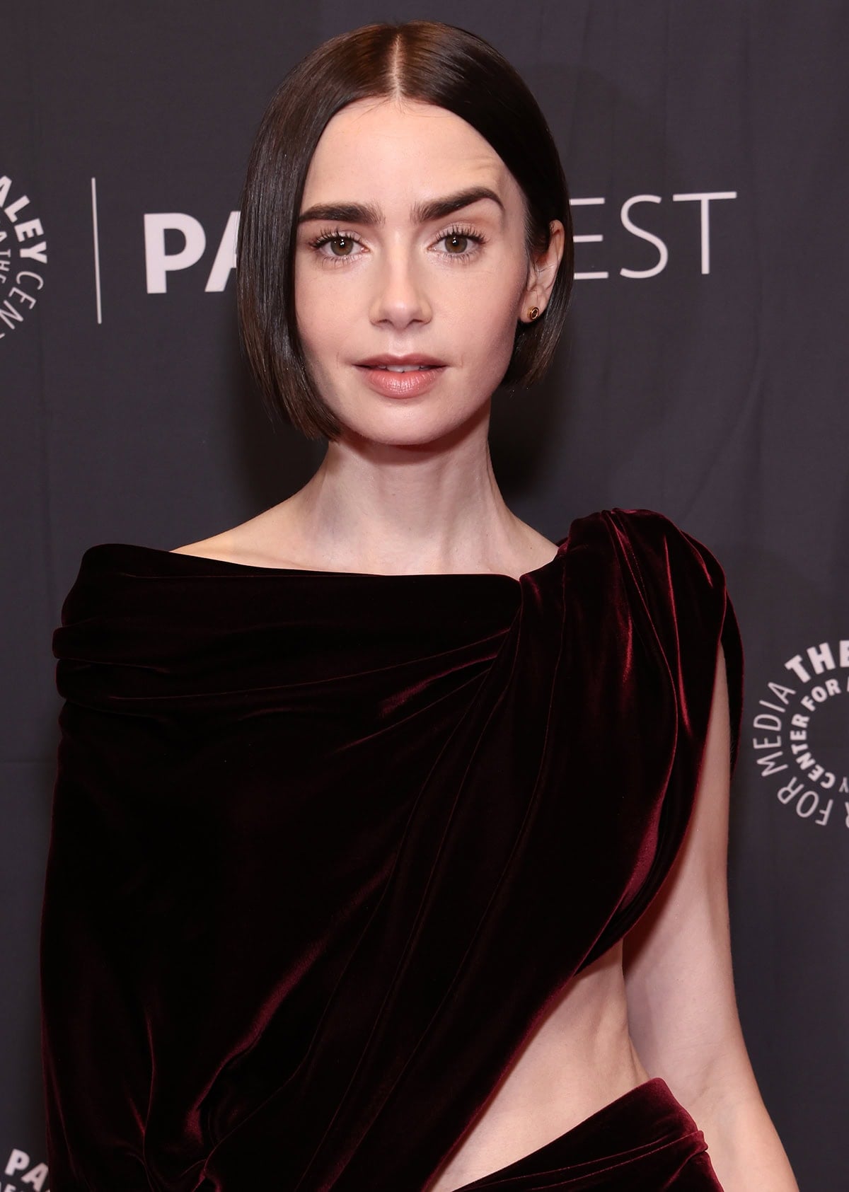 Lily Collins styles her bob hair straight and tucked behind one ear, showcasing her Cartier Love stud earrings