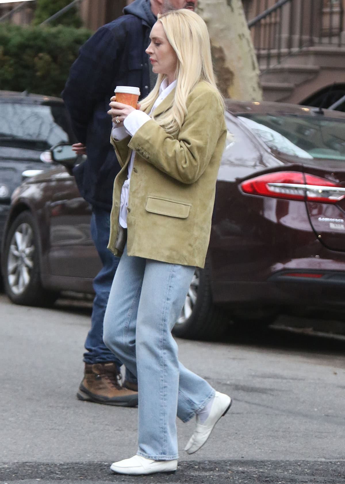Lindsay Lohan pairs her white loafers with light-wash denim jeans, a white shirt with a waist tie, and a green suede jacket