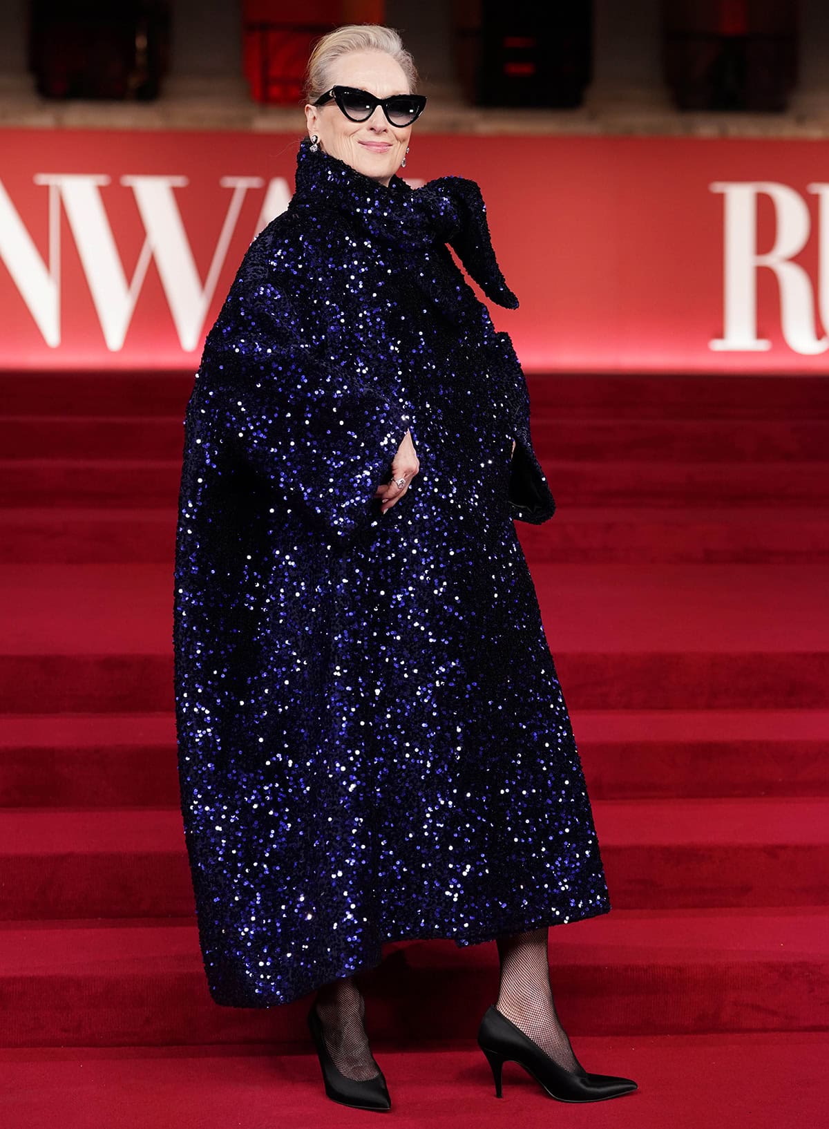 Meryl Streep pairs her classic black pumps with fishnets and a voluminous cape-like gown by Richard Quinn, embellished with midnight blue sequins all over