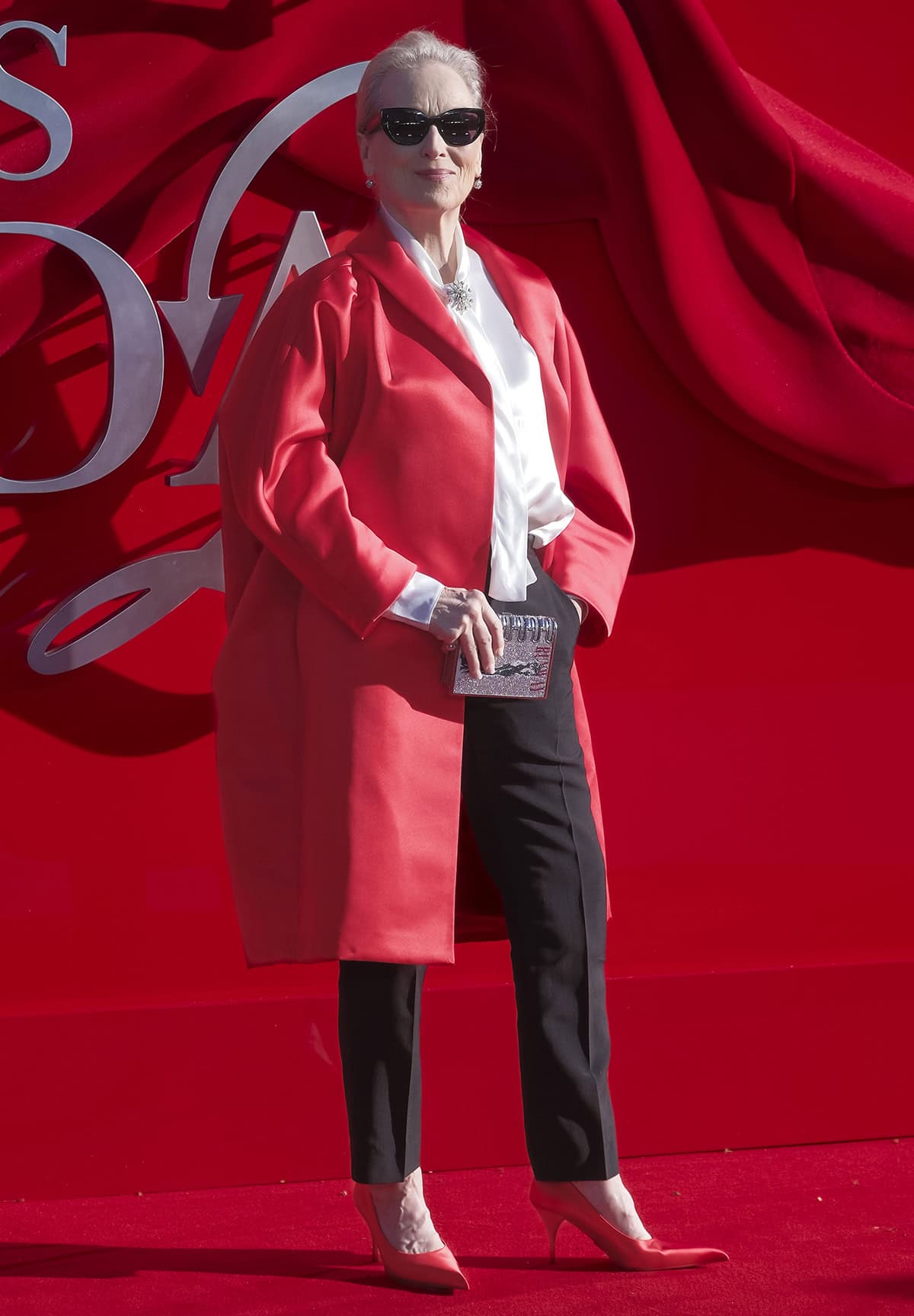 Meryl Streep pairs her red pumps with black trousers, a white silk blouse with a scarf, and a red satin Prada car coat