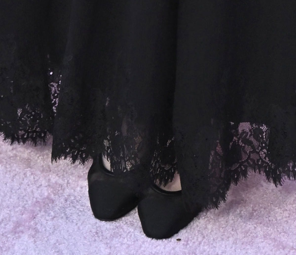 Sadie Sandler wears black mesh pumps with leather trims and cap toes, adding subtle texture and contrast beneath her lace-trimmed hem