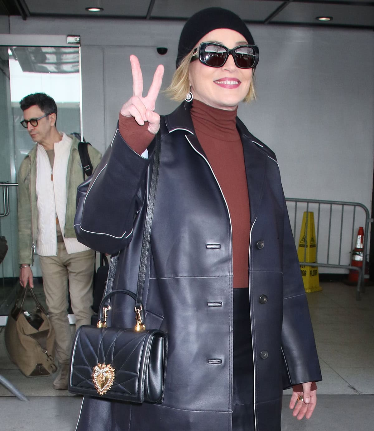 Sharon Stone styles her already bold ensemble with a Dolce & Gabbana bag, a beanie, drop earrings, and black sunglasses
