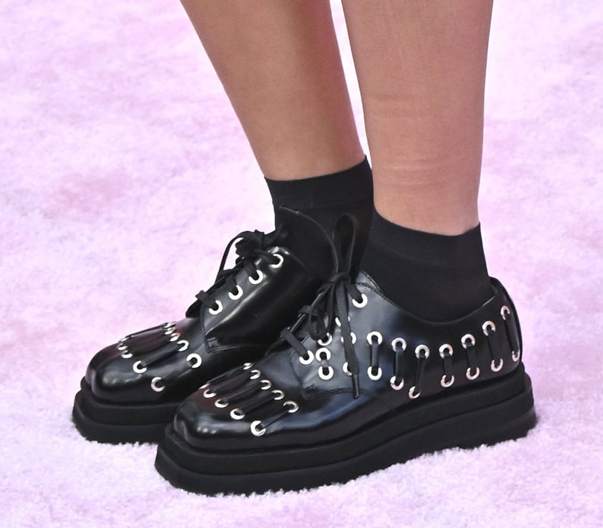Xochitl Gomez wears a pair of black leather brogues by Simone Rocha featuring silver-tone grommets, leather laces, and chunky platforms