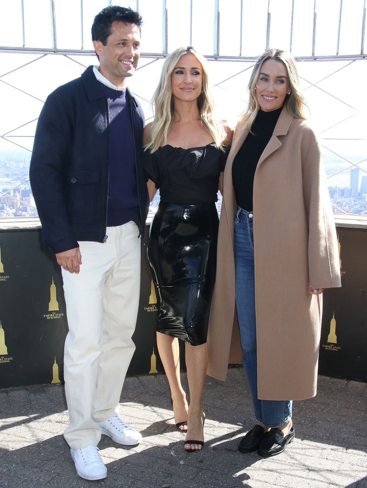 Kristin Cavallari sharpens her glossy PVC look with minimal black slingback heels, while Lauren Conrad keeps it effortless in black Rag & Bone mules alongside Stephen Colletti’s clean white sneakers at the Empire State Building on April 7, 2026, in New York City
