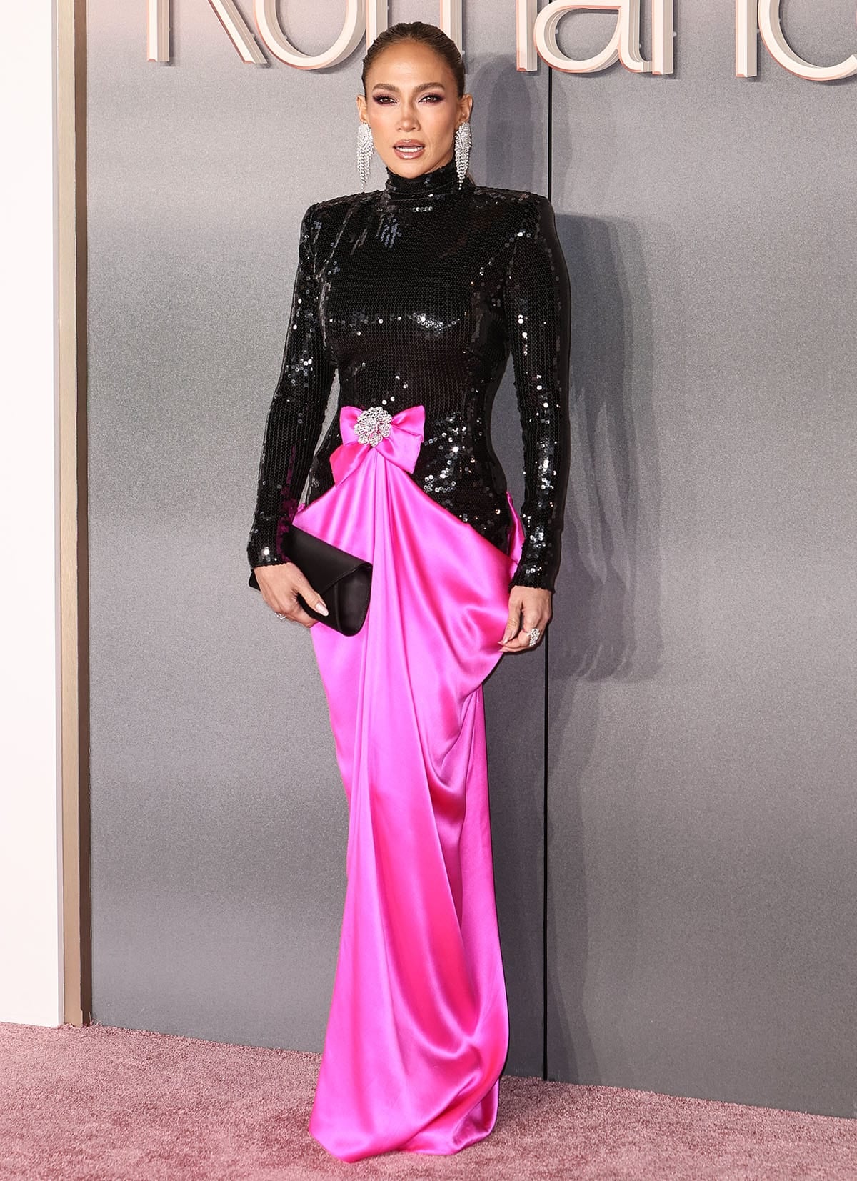 Jennifer Lopez embraces Barbiecore in a black sequined long-sleeved top and a hot pink satin draped skirt with a pink bow at the waist by Richard Quinn at the UK premiere of Office Romance