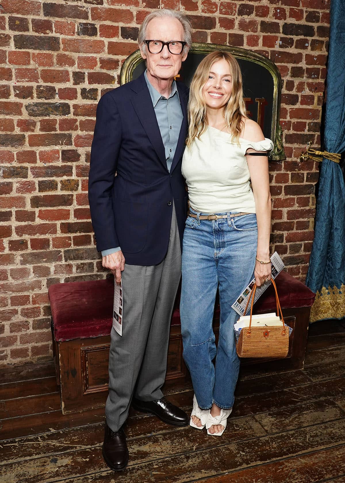 Sienna Miller, with Bill Nighy, attends the London Press Night for Midnight At The Never Get at the Chocolate Factory in an asymmetrical top, jeans, and white Givenchy heels